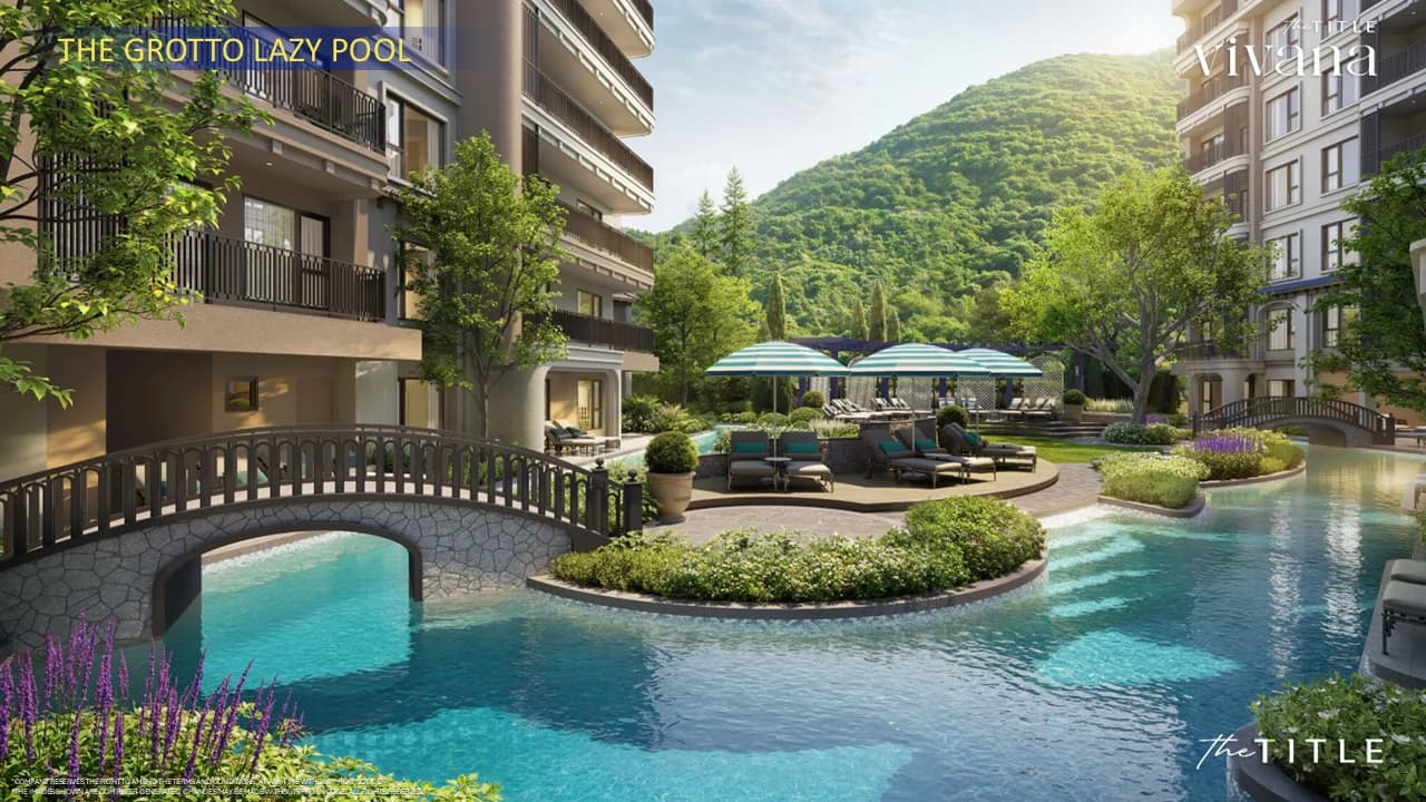 The Grotto lazy pool at eye level: a stone bridge, an island with loungers and the jungle hill behind the buildings